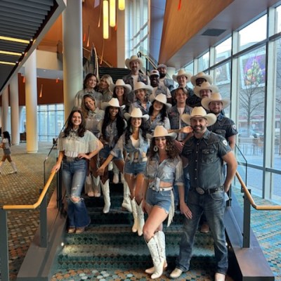 Group of people in cowboy hats and boots posing on a staircase indoors.