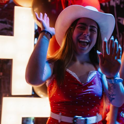 Smiling woman in red dress and white cowboy hat waving at a party.