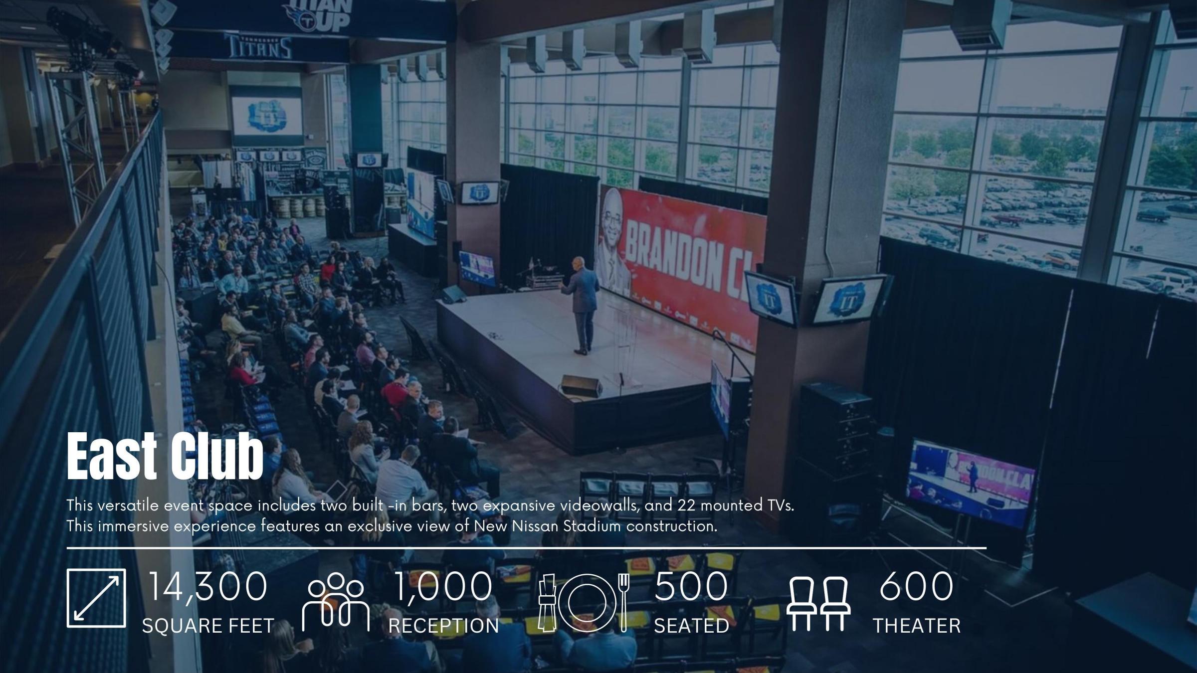 Event space in a stadium with a speaker on stage, seating area, and large screens on walls.